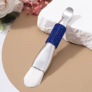 Close-up detail of double-headed silver mask brush with blue rhinestone handle and soft bristles