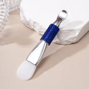 Detail of double-ended silicone mask brush with blue rhinestone handle and metal spatula.
