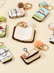 Detail view of mini notebook keychain with cute cat illustration and soft plush ball charm.