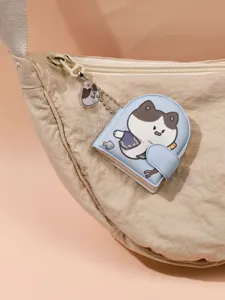 Close-up view of a cute mini cat cartoon notebook pendant keychain hanging on a beige fabric bag.
