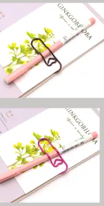 Nahaufnahme eines herzförmigen Metall-Stifthalters, der einen rosa Stift am Notizbuch hält