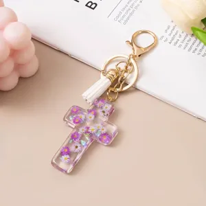 Detailed view of a clear resin cross keychain with purple flowers and a white tassel