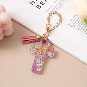 Close-up of a resin cross keychain filled with colorful dried flowers and a pink tassel
