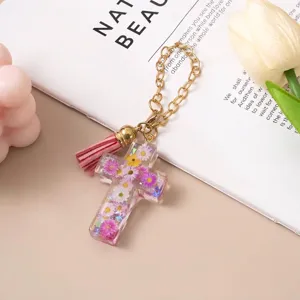 Close-up of a floral resin cross keychain with a pink tassel and gold chain pendant