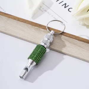 Detailed view of a silver aluminum survival whistle with green rhinestones and keyring.