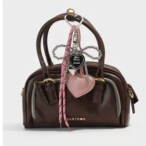 Detailansicht des herzförmigen Taschenanhängers und der rosa Kordel an der braunen Tasche