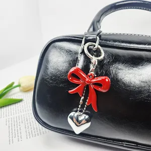 Close-up detail of a glossy red bow and silver heart keychain on a black leather bag