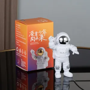 Close-up of a cute white astronaut figurine with silver helmet beside its orange packaging box.