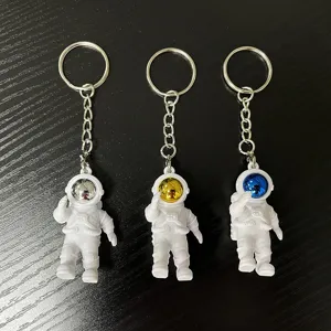 Detailed view of three cute astronaut keychains with silver, gold, and blue visors on dark table.