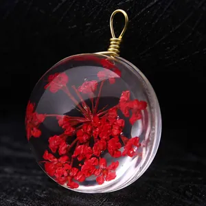 Macro view showing a clear resin pendant with red dried flowers and a gold wire loop.