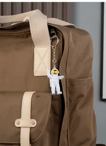 Brown canvas backpack with astronaut keychain pendant, stylish student school bag.