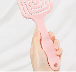 Pink curved hair brush detail close-up showing ergonomic handle and wide teeth design.