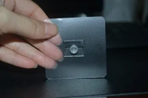Detalle de soporte de gancho de pared autoadhesivo transparente con base cuadrada.