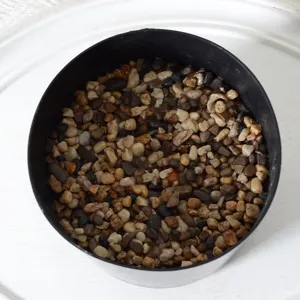 Black plastic flower pot filled with decorative small stones for artificial plants setup.