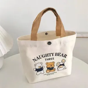 Detailed view of white canvas tote bag with cute cartoon bear print and brown handles.