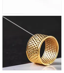 Gold sewing thimble ring detail view with needle for manual embroidery and craft work.