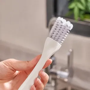 Gros plan de la brosse de nettoyage de cuisine avec manche blanc et poils denses.