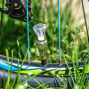 Detailopname van een diamantvormig LED fietsventieldoplicht gemonteerd op een wiel in gras.