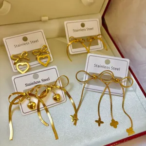 Detailansicht goldener Edelstahlohrringe mit Schleifen und Herzanhängern in Geschenkbox