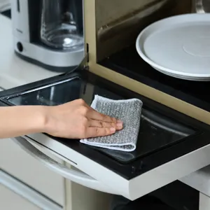 Close-up detail shot of a silver wire dishcloth cleaning a microwave oven door easily.