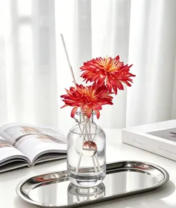 Set de difusor con flores artificiales rojas, botella de vidrio y etiqueta decorativa.