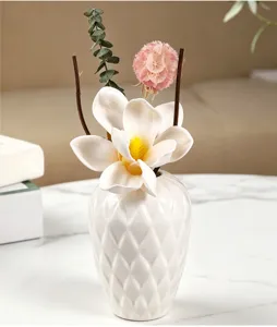 Primer plano detallado de un florero de cerámica blanca con flores secas y decoracion.