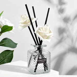 Elegante botella difusora de aromas de vidrio con varillas negras y flores de rosas blancas.