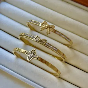 Dettaglio di tre bracciali in acciaio al titanio dorato con motivi a fiocco e floreali