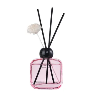 Pink glass bottle reed diffuser with black sticks and flower for home fragrance air freshener.