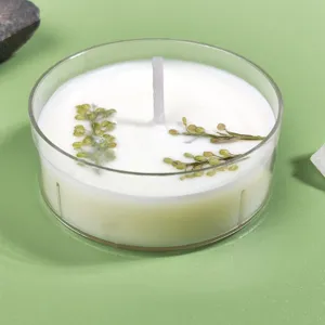 Close-up detail of scented tea wax candle in clear cup with dried green floral botanicals.