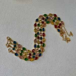 Close-up detail of gold-tone bracelets featuring vibrant multi-color teardrop stones