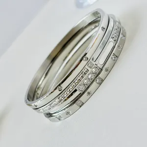 Dettaglio macro di tre braccialetti in acciaio titanio argento con pietre di zircone.