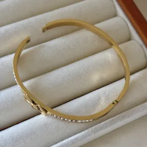 Elegante bracciale a rigido con fiocco in acciaio titanio dorato e cristalli brillanti.