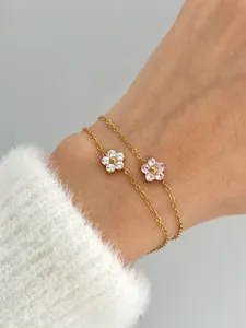 Close-up of delicate gold flower bracelets with pink and white zircon stones on wrist.
