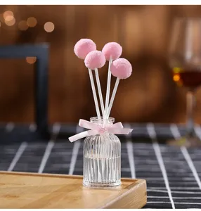 Close up of decorative reed diffuser glass bottle with pink pom pom sticks for home decor aroma.
