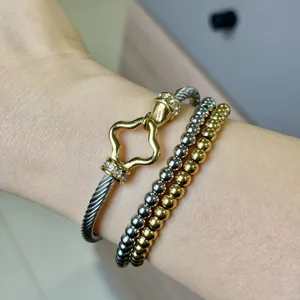Close-up of two-tone cable bangle with clover clasp and beaded bracelets on wrist
