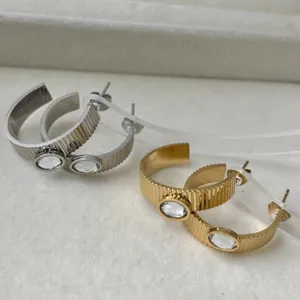Dettaglio orecchini a cerchio C in acciaio rigato con cristalli ovali oro e argento.