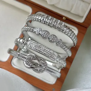 Stack of four silver stainless steel bangles featuring a knotted design and sparkling stones