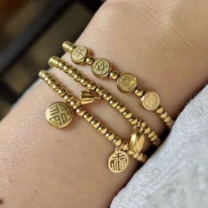 Dettaglio macro di braccialetti con perline d'oro in acciaio da 3 mm e ciondoli portafortuna