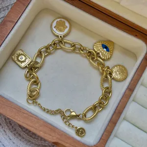 Gedetailleerd aanzicht van 18K gouden bedelarmband met Hamsa en boze oog in houten doos