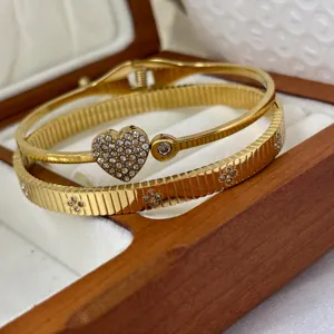 Nahaufnahme goldener Edelstahlarmbänder mit Herz- und Kleeblatt-Diamantdetails.
