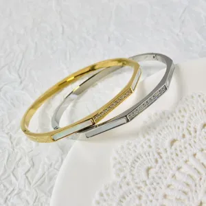 Dettaglio di eleganti bracciali rigidi geometrici oro e argento con conchiglia e zirconi.
