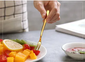 Detailed view of a golden stainless steel fruit fork piercing a cherry tomato in a sweet dessert.