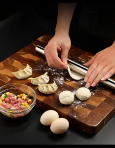 Close-up of stainless steel rolling pin flattening dough on wooden kitchen cutting board.