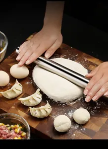Stainless steel rolling pin detail showing smooth metal cylinder flattening fresh dough.
