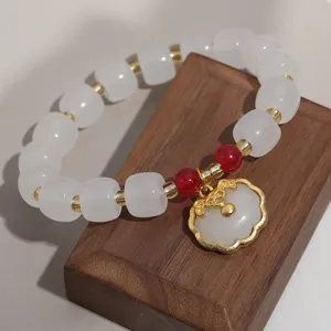 Gros plan détaillé du bracelet de perles blanches avec pierre rouge et pendentif ruyi doré.
