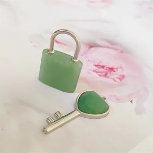 Detailansicht eines grünen Naturstein-Schlosses und Herz-Schlüssel-Anhängers auf Blumenstoff.