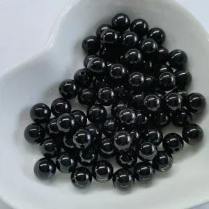 Close-up detail of smooth black round beads in a white dish, ideal for DIY jewelry making.