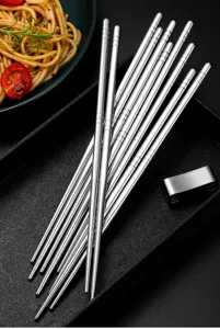 Close-up detail of stainless steel square chopsticks set with metal rest and food props.