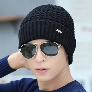 Close-up detail of mens black knitted beanie hat with metal NY logo and winter style.